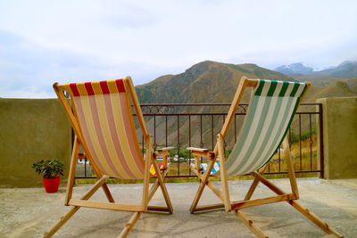 Empty chairs on beach against sky