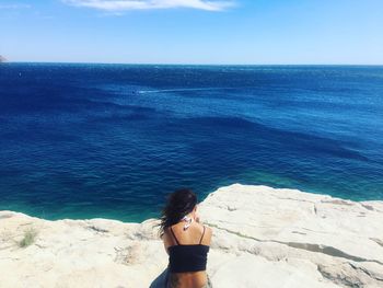 Rear view of woman sitting on rock against sea