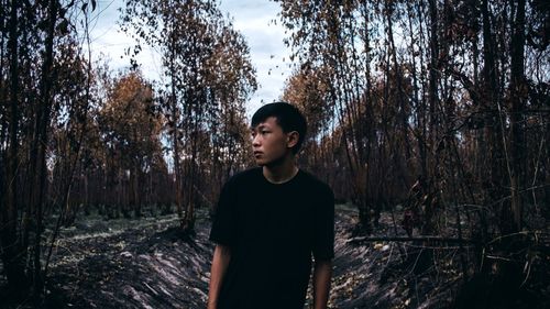 Young woman standing by trees in forest against sky