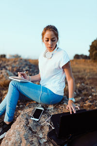 Young woman wearing headphones sitting on field