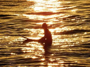 Silhouette person sitting in sea during sunset