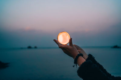 Person holding sea against sky during sunset