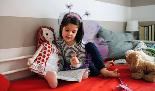 Girl in fairy costume with toy reading book bed at home