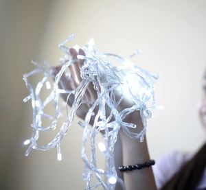 Midsection of woman holding string lights against wall