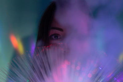 Close-up portrait of young woman holding multi colored fiber optic with smoke