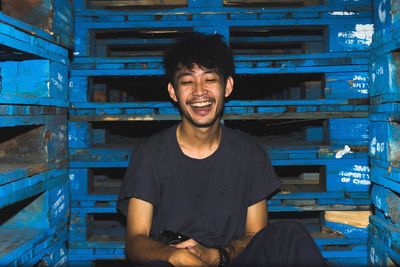 Happy young man sitting against wooden racks