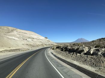 Road leading towards mountains against clear blue sky