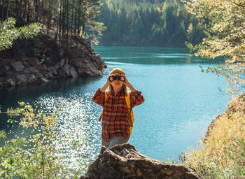 Young caucasian woman with binoculars by lake or river looking at birds migration in fall  birding