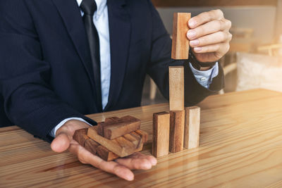 Midsection of businessman stacking wooden toy blocks on table