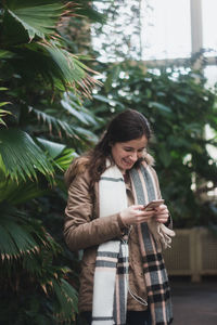 Smiling woman using phone while standing on tree