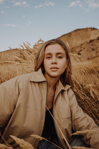 Portrait of young woman sitting by plants against sky