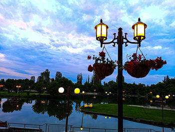 Illuminated street light by lake against sky at dusk