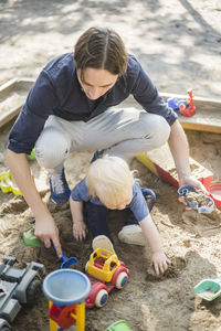 High angle view of father and son playing with toys on sand in playground at park