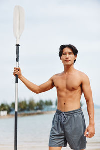 Portrait of shirtless young man standing against sky