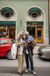 Full length of senior man and woman standing with smart phone against building in city