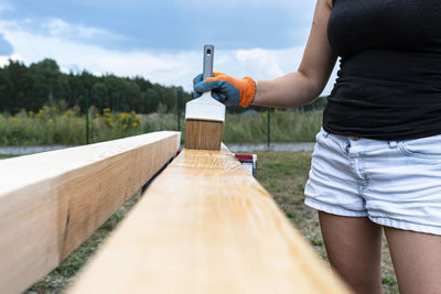The woman impregnates raw planed wooden pine beams with dimensions 100mm with colorless impregnation