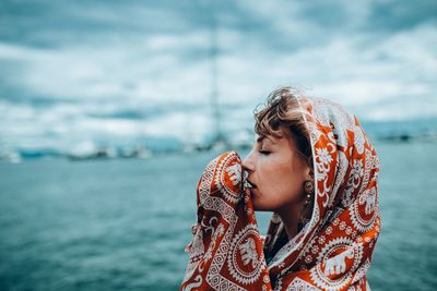 Profile view of young woman wearing headscarf by sea