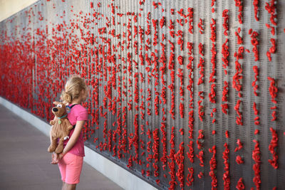 Side view of girl with backpack standing by wall