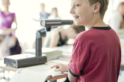 Happy boy reading book under camera on desk at classroom
