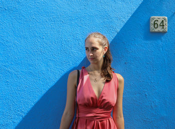 Portrait of young woman standing against blue wall