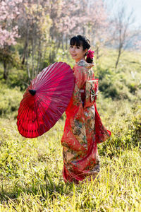 Woman with red umbrella standing by plants