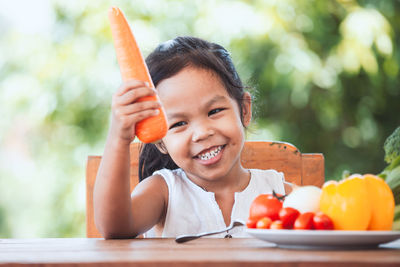 Smiling girl holding carrot at home