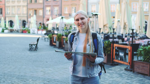 Portrait of smiling young woman holding umbrella on street in city