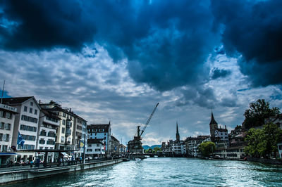 View of city at waterfront against cloudy sky