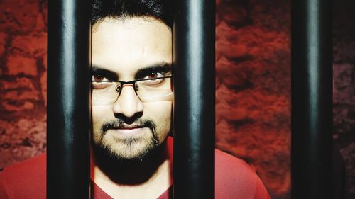 Portrait of young man standing behind security bar