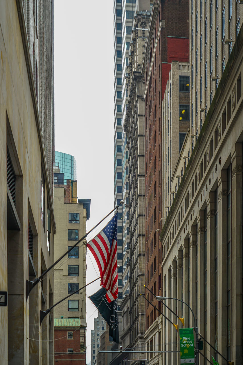 LOW ANGLE VIEW OF FLAG AGAINST BUILDINGS IN CITY AGAINST SKY