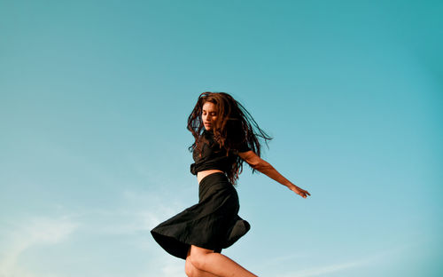 Low angle view of woman standing against blue sky