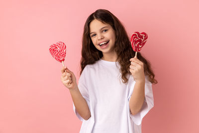 Portrait of woman holding heart shape against pink background