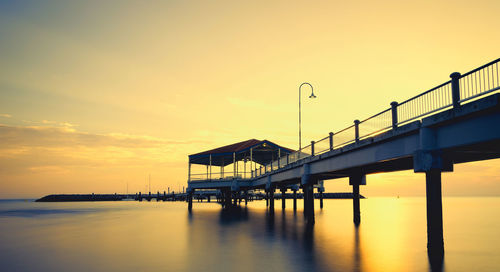 Silhouette bridge over sea against sky during sunset
