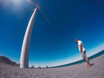 Low angle view of man standing by windmill against clear blue sky