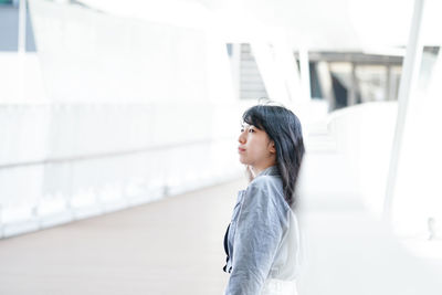 Side view of young woman standing against built structure