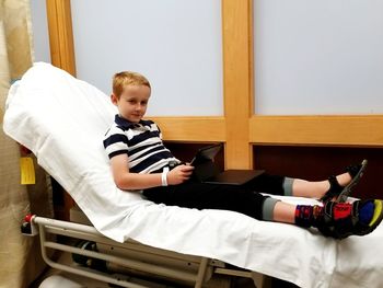 Portrait of boy with digital tablet sitting on bed in hospital