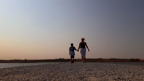 Rear view of friends on land against sky during sunset