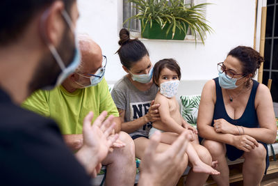 A baby wearing a mask while being watched by the whole family. concept family