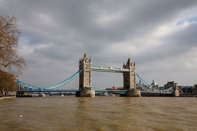 View of suspension bridge over river against cloudy sky