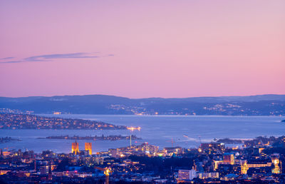 High angle view of illuminated buildings by sea against sky at sunset