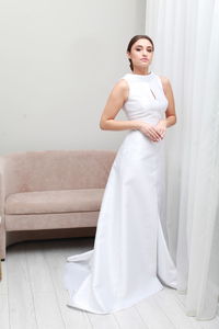 Full length portrait of bride in elegant wedding dress posing at home, pensive expression 