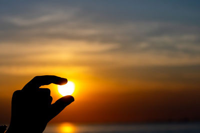 Silhouette hand against sky during sunset