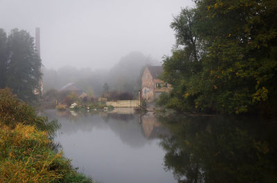 Scenic view of lake by trees against sky during foggy weather