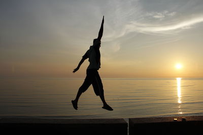 Silhouette man in sea against sky during sunset