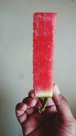 Cropped image of person holding watermelon slice against wall