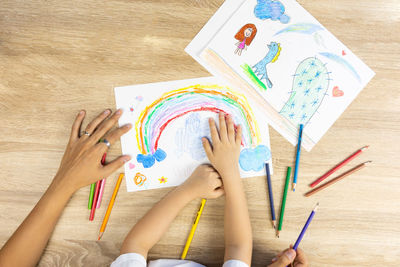 Top view shot of mother and daughter are drawing and coloring beautiful rainbow picture on paper 