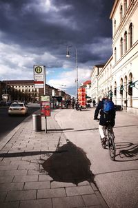 People walking on city street against cloudy sky