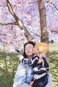 A boy kissed his mom. they were under pink sakura blossom. it was april in spring time. 