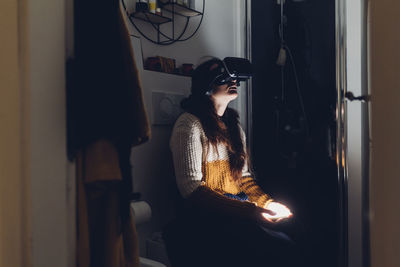 Woman with virtual reality headset sitting in toilet at home