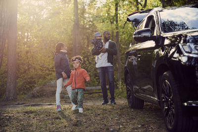 Full length of father with children standing by car against trees in forest